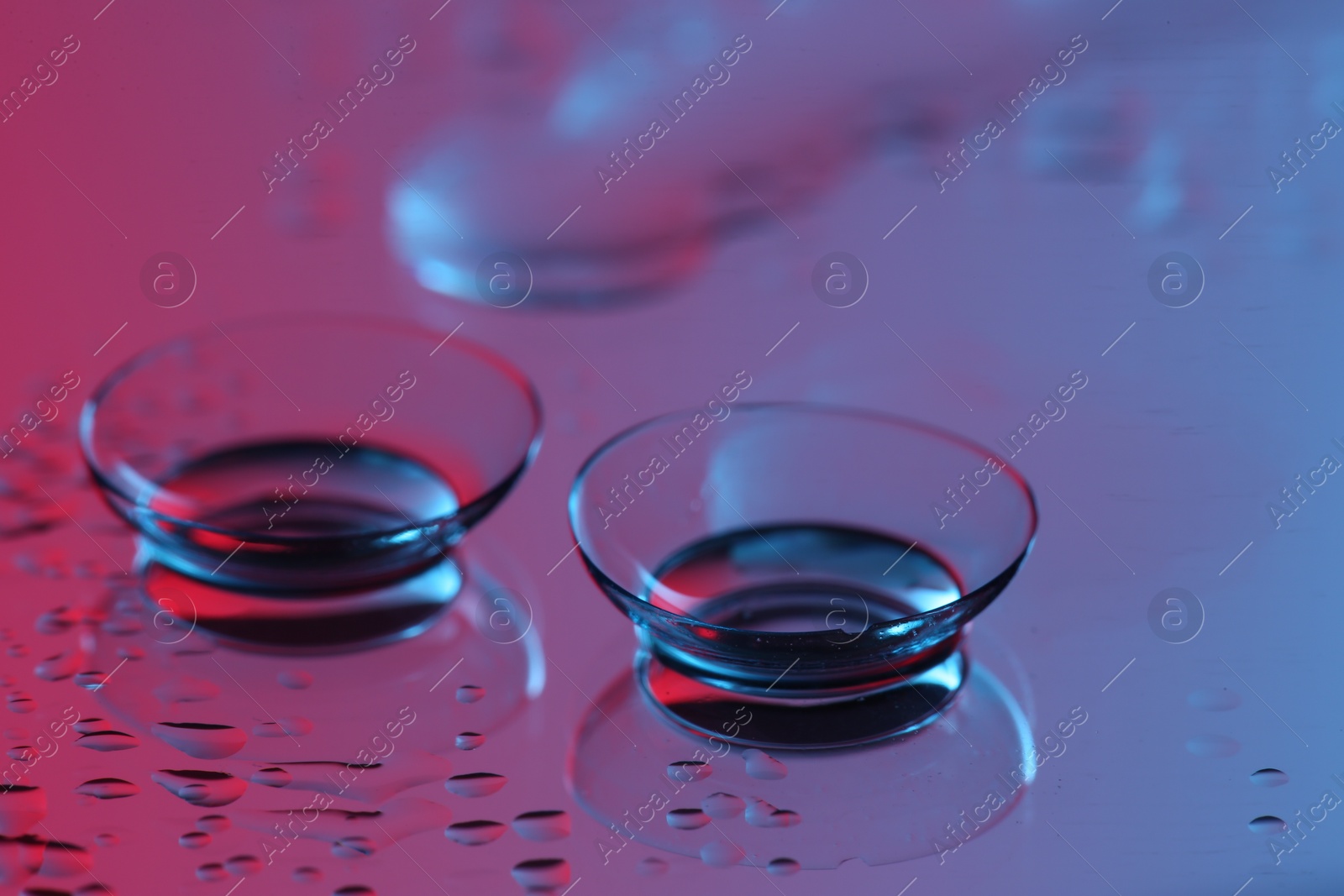 Photo of Pair of contact lenses on wet mirror surface, closeup