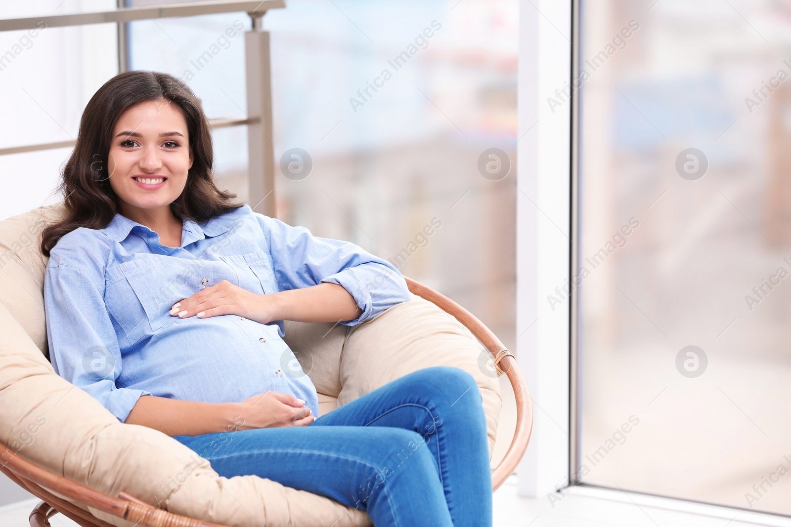 Photo of Beautiful pregnant woman sitting in lounge chair near window