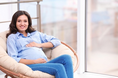 Photo of Beautiful pregnant woman sitting in lounge chair near window