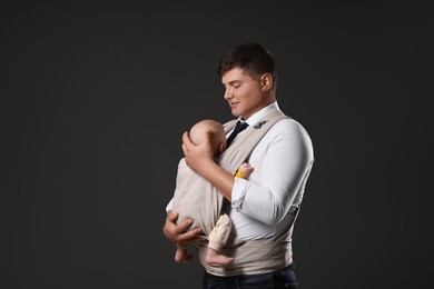 Father holding his child in baby carrier on black background