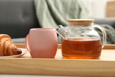 Photo of Aromatic tea in teapot, cup and tasty croissant on table indoors