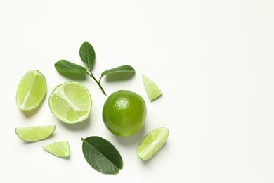 Whole and cut fresh ripe limes with green leaves on white background, flat lay