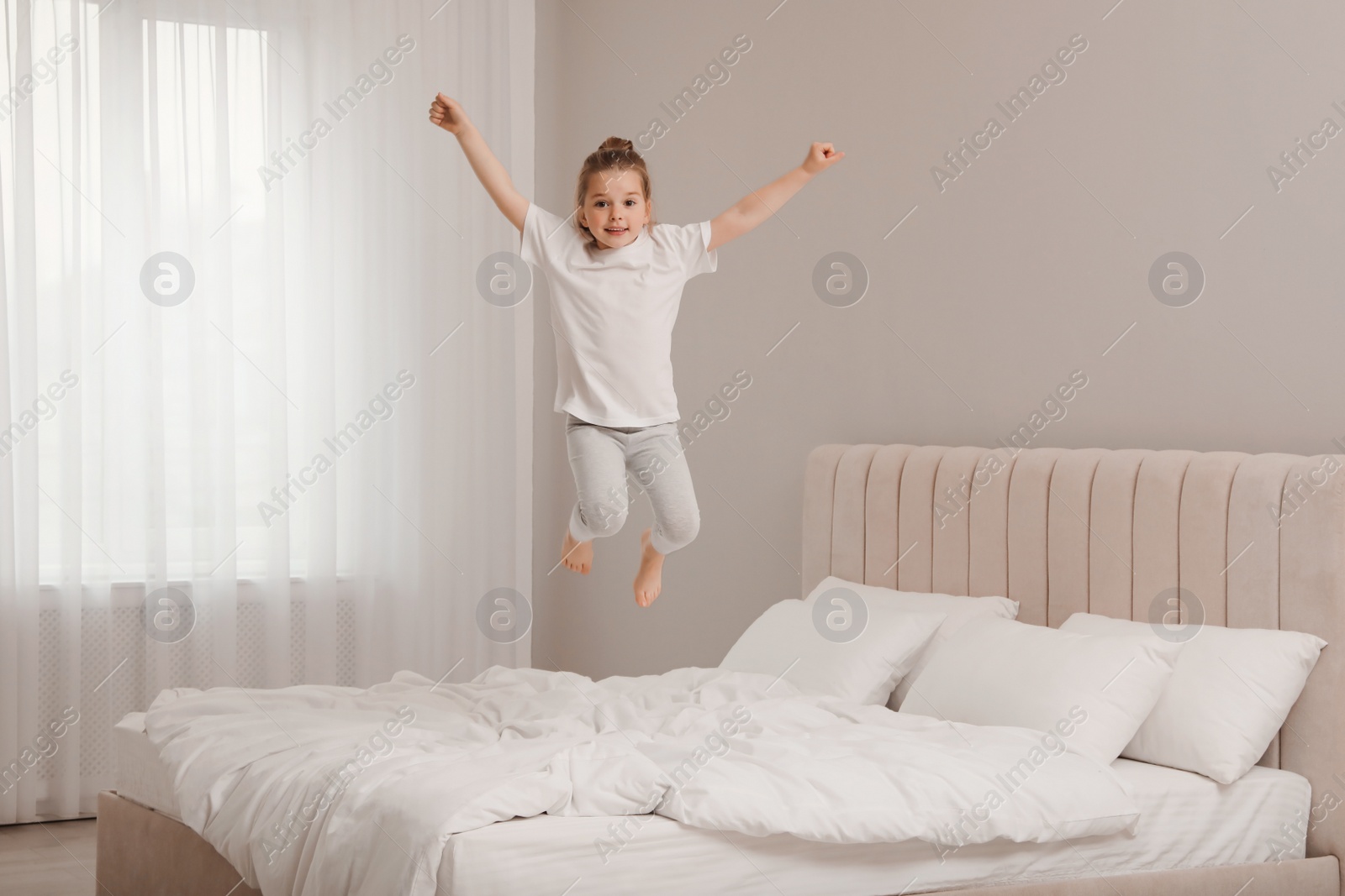 Photo of Cute little girl jumping on bed at home