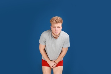 Young man suffering from pain on blue background. Urology problems