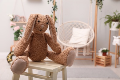 Photo of Cute toy rabbit on wooden stand in room. Space for text