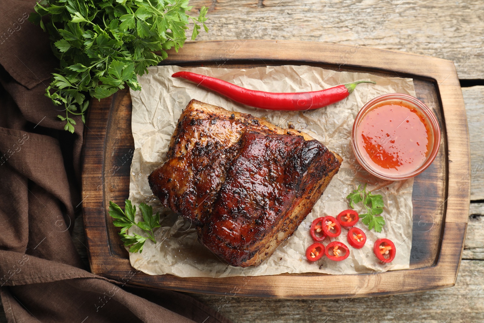 Photo of Piece of baked pork belly served with sauce and chili pepper on wooden table, top view