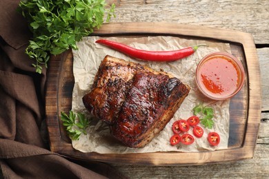 Photo of Piece of baked pork belly served with sauce and chili pepper on wooden table, top view