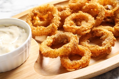 Photo of Homemade crunchy fried onion rings and sauce on wooden dish, closeup