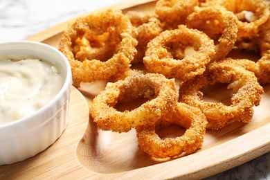 Homemade crunchy fried onion rings and sauce on wooden dish, closeup