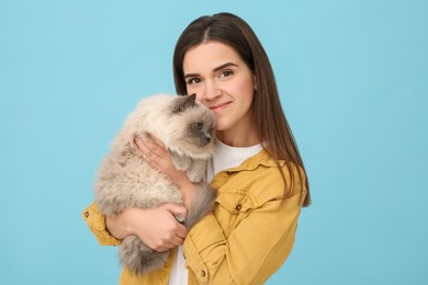 Photo of Woman hugging her cute cat on light blue background