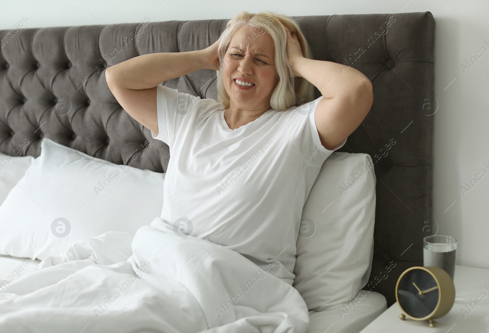 Photo of Mature woman suffering from headache while sitting in bed indoors