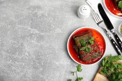 Photo of Plate of delicious stuffed grape leaves with tomato sauce, parsley and cutlery on light grey table, flat lay. Space for text