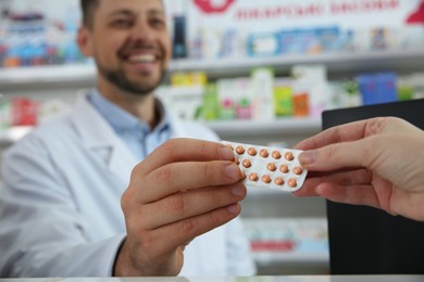 Professional pharmacist giving pills to customer in drugstore, closeup