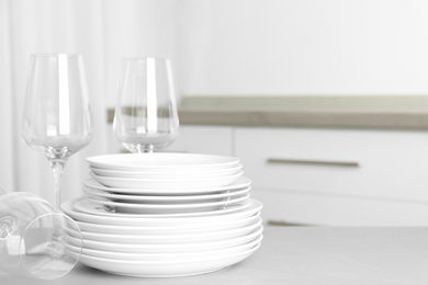 Photo of Stack of clean plates and glasses on grey table in kitchen. Space for text