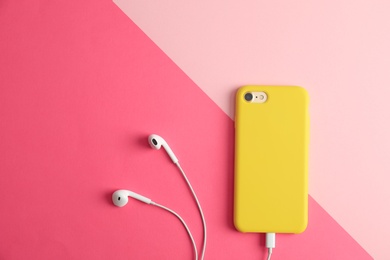 Photo of Modern phone with earphones on color background, top view. Space for text