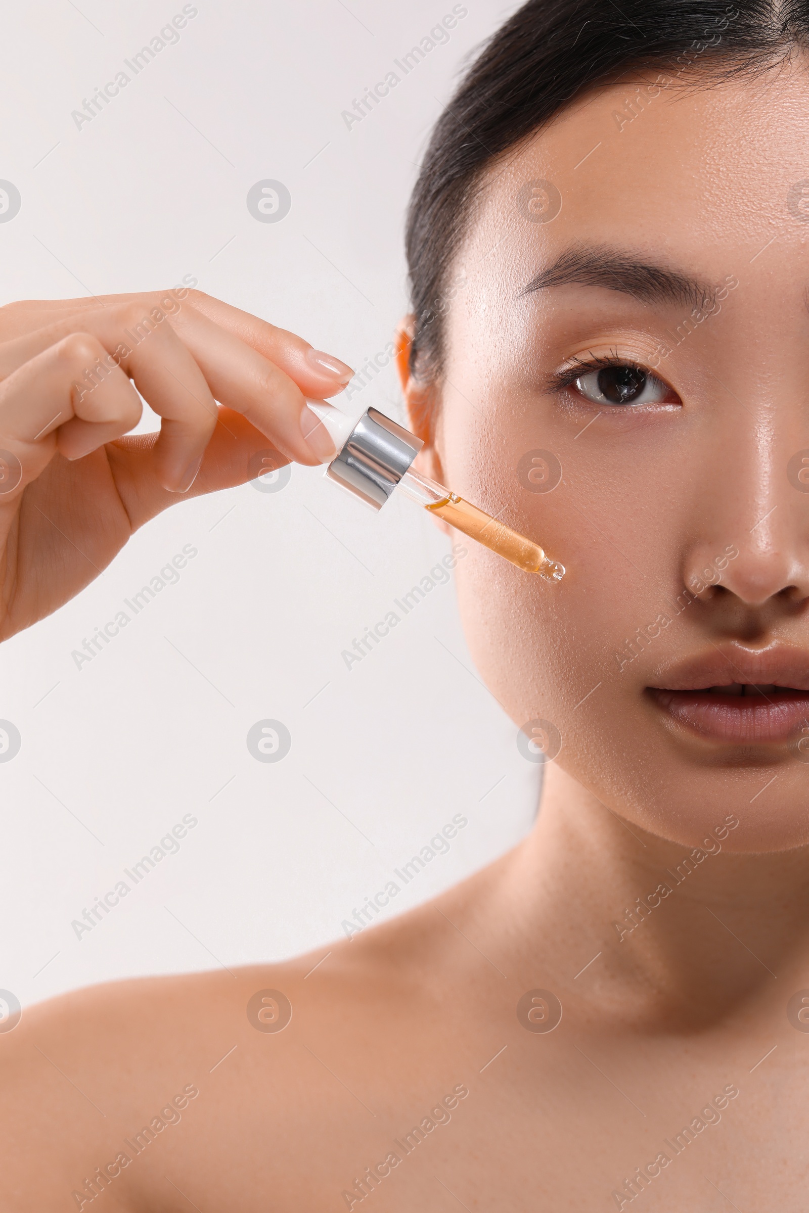 Photo of Beautiful young woman applying cosmetic serum onto her face on white background, closeup