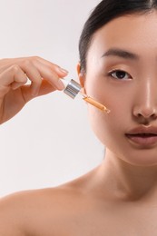 Beautiful young woman applying cosmetic serum onto her face on white background, closeup