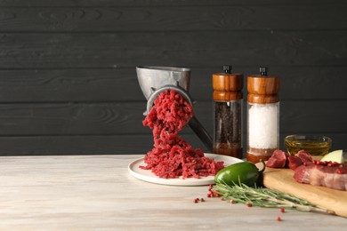 Photo of Metal meat grinder with minced beef, products and spices on light wooden table. Space for text