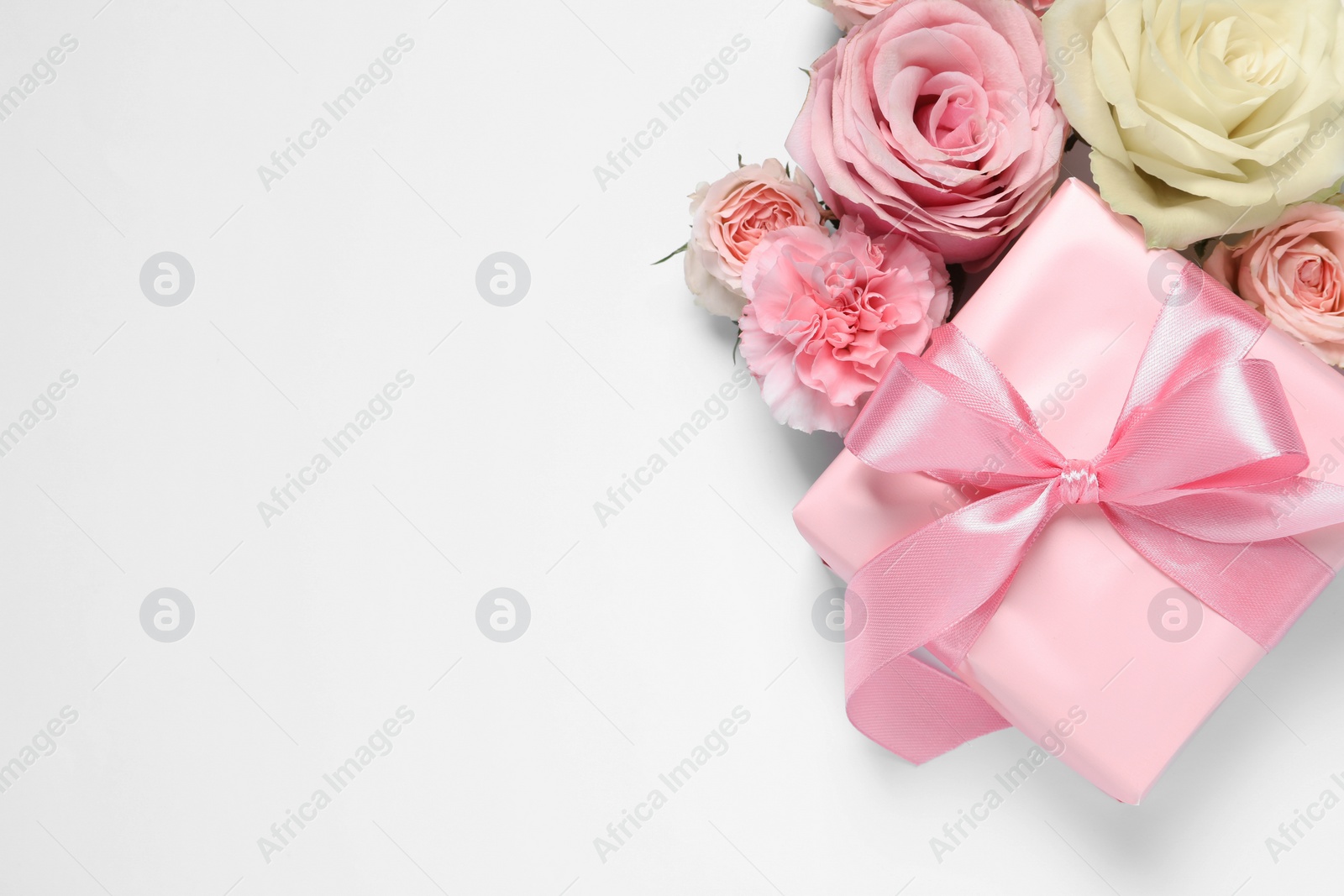 Photo of Gift box and beautiful flowers on white background, flat lay. Space for text