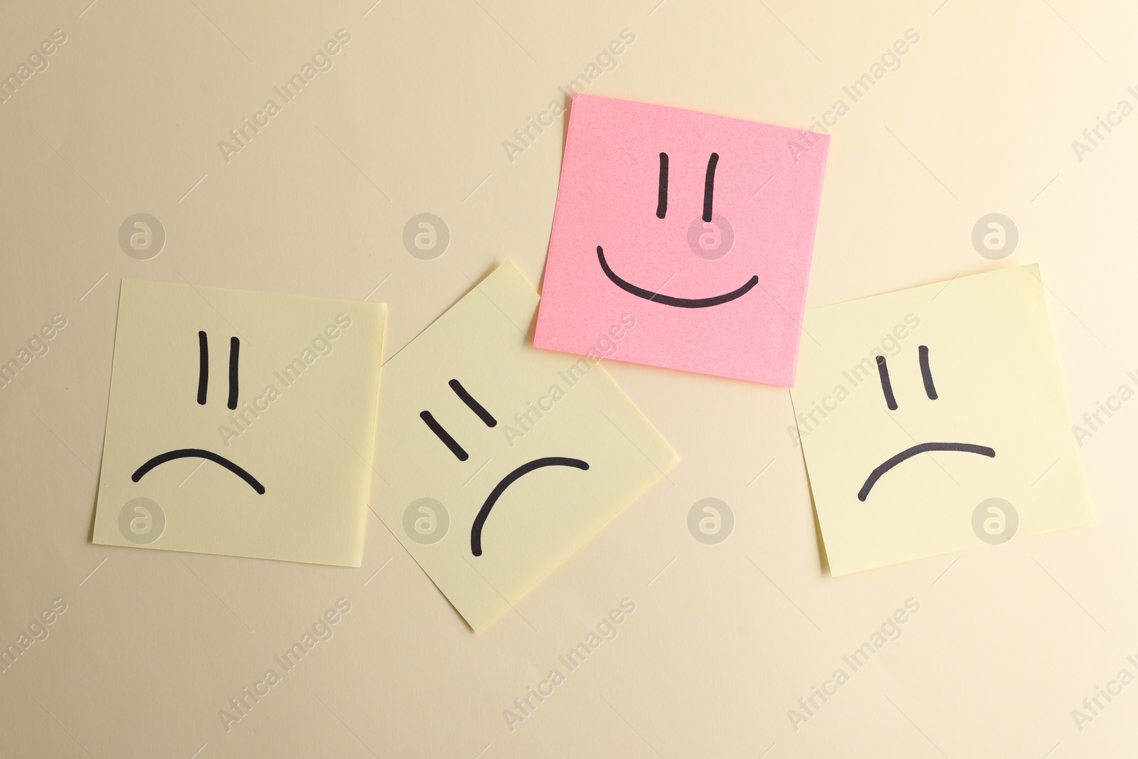 Photo of Choice concept. Pink sticky note with happy emoticon among yellow papers with sad emojis on beige background, top view