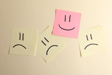 Choice concept. Pink sticky note with happy emoticon among yellow papers with sad emojis on beige background, top view