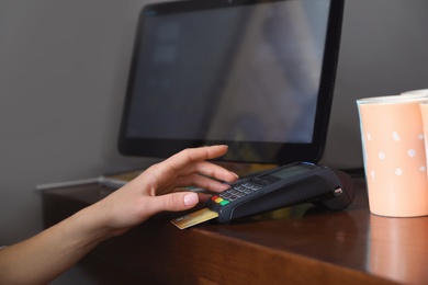 Woman using credit card machine for non cash payment in cafe, closeup