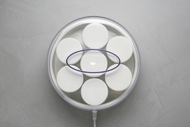 Modern yogurt maker with jars on light grey table, top view