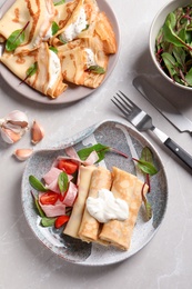 Photo of Thin pancakes served with sour cream and garnish on plates, top view