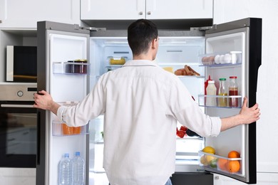 Man near refrigerator in kitchen at home, back view