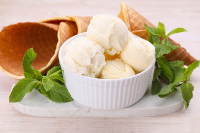Photo of Bowl of ice cream and mint leaves on light wooden table, closeup