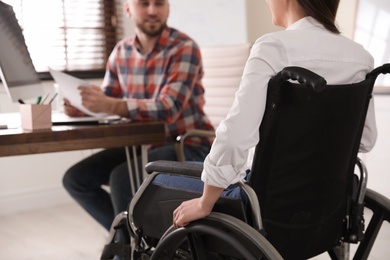 Woman in wheelchair with her colleague at workplace, closeup