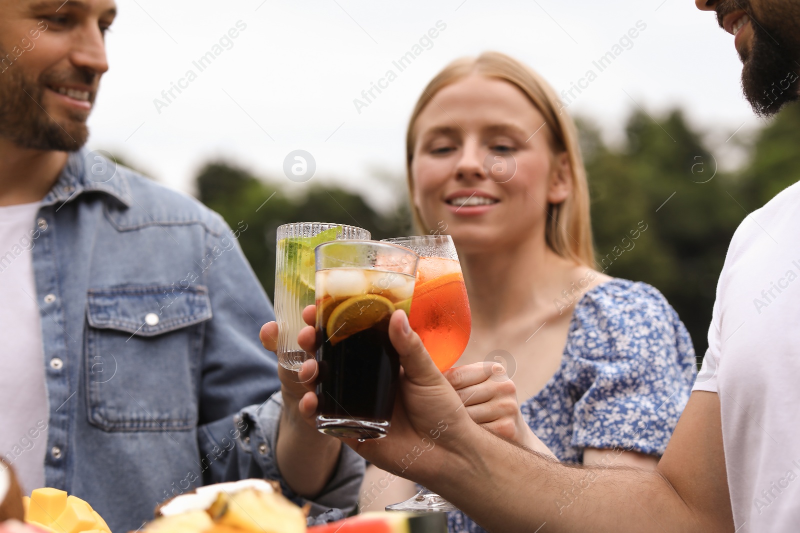 Photo of Happy friends clinking glasses with cocktails outdoors, selective focus