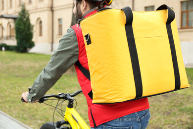 Courier with thermo bag riding bicycle outdoors, closeup. Food delivery service