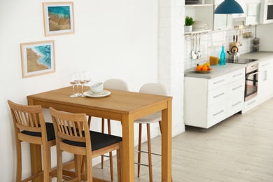 Stylish kitchen interior with dining table and bar stools near white wall