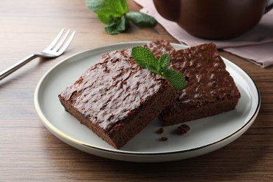 Photo of Delicious chocolate brownies with fresh mint served on wooden table, closeup