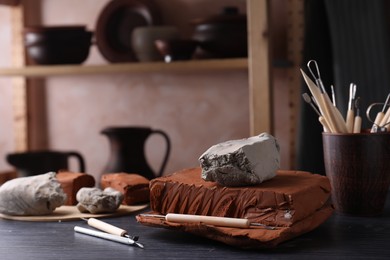 Photo of Clay and set of modeling tools on dark gray wooden table in workshop