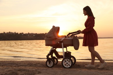 Photo of Happy mother with baby in stroller walking near river at sunset