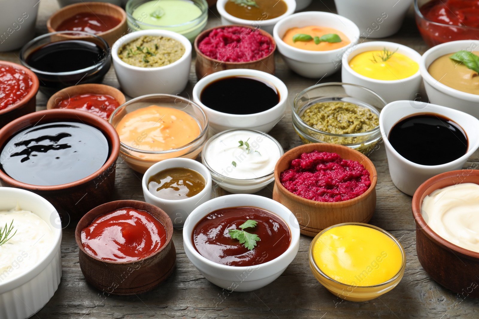 Photo of Many bowls with different sauces and herbs on wooden table