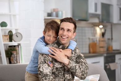 Photo of Young man in military uniform with his little son at home