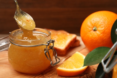 Photo of Spoon with delicious orange marmalade over jar near fresh fruits on table, closeup