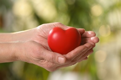 Photo of Elderly woman holding red heart in hands on blurred green background, closeup