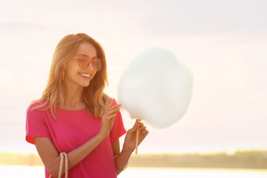 Photo of Happy young woman with cotton candy outdoors