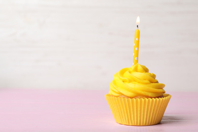 Photo of Delicious birthday cupcake with cream and burning candle on pink table. Space for text