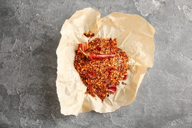 Photo of Parchment with crushed chili pepper and pod on grey background