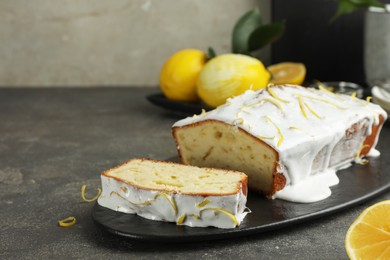 Photo of Tasty lemon cake with glaze and citrus fruits on gray table, closeup. Space for text