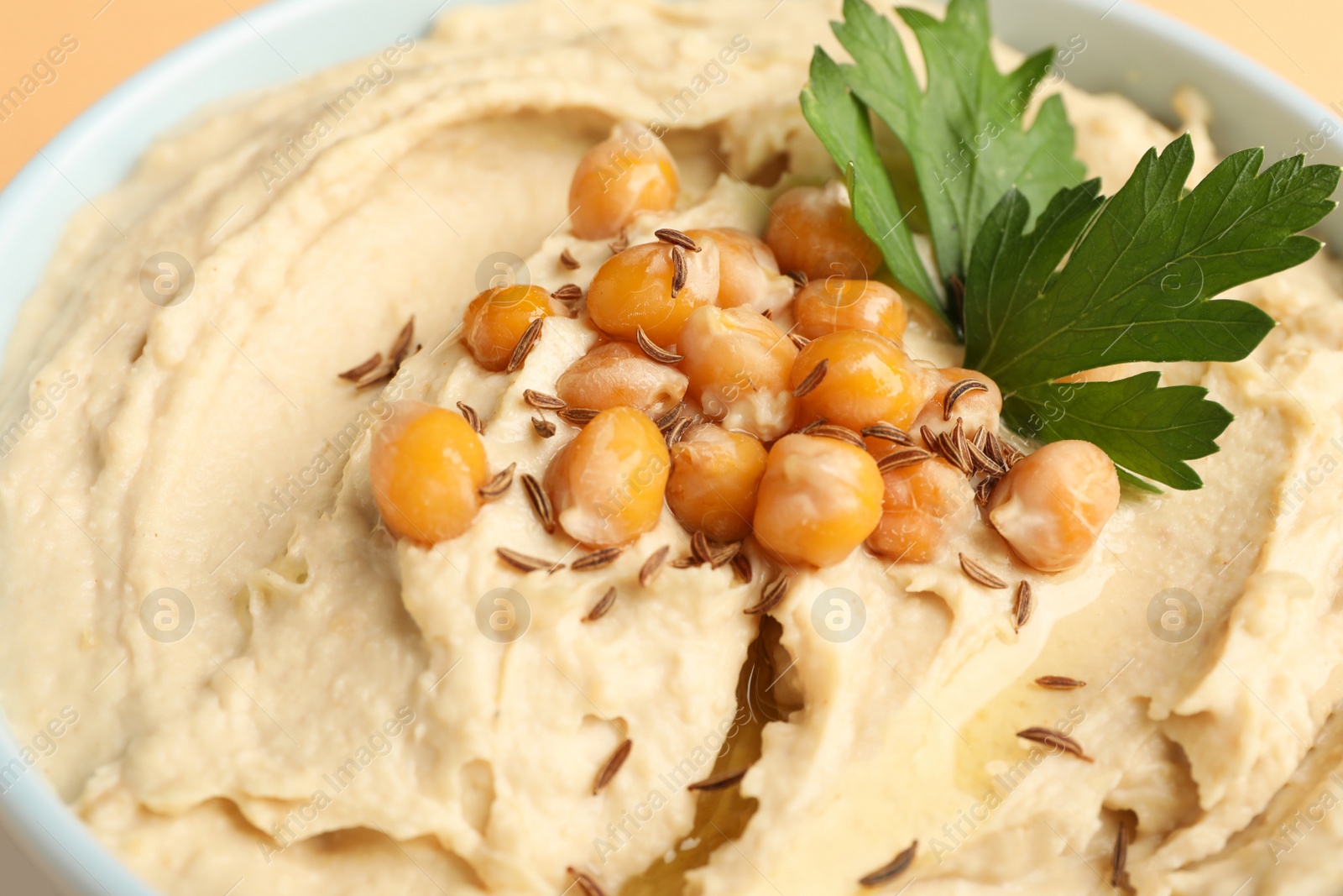 Photo of Bowl of tasty hummus with chickpeas and parsley, closeup