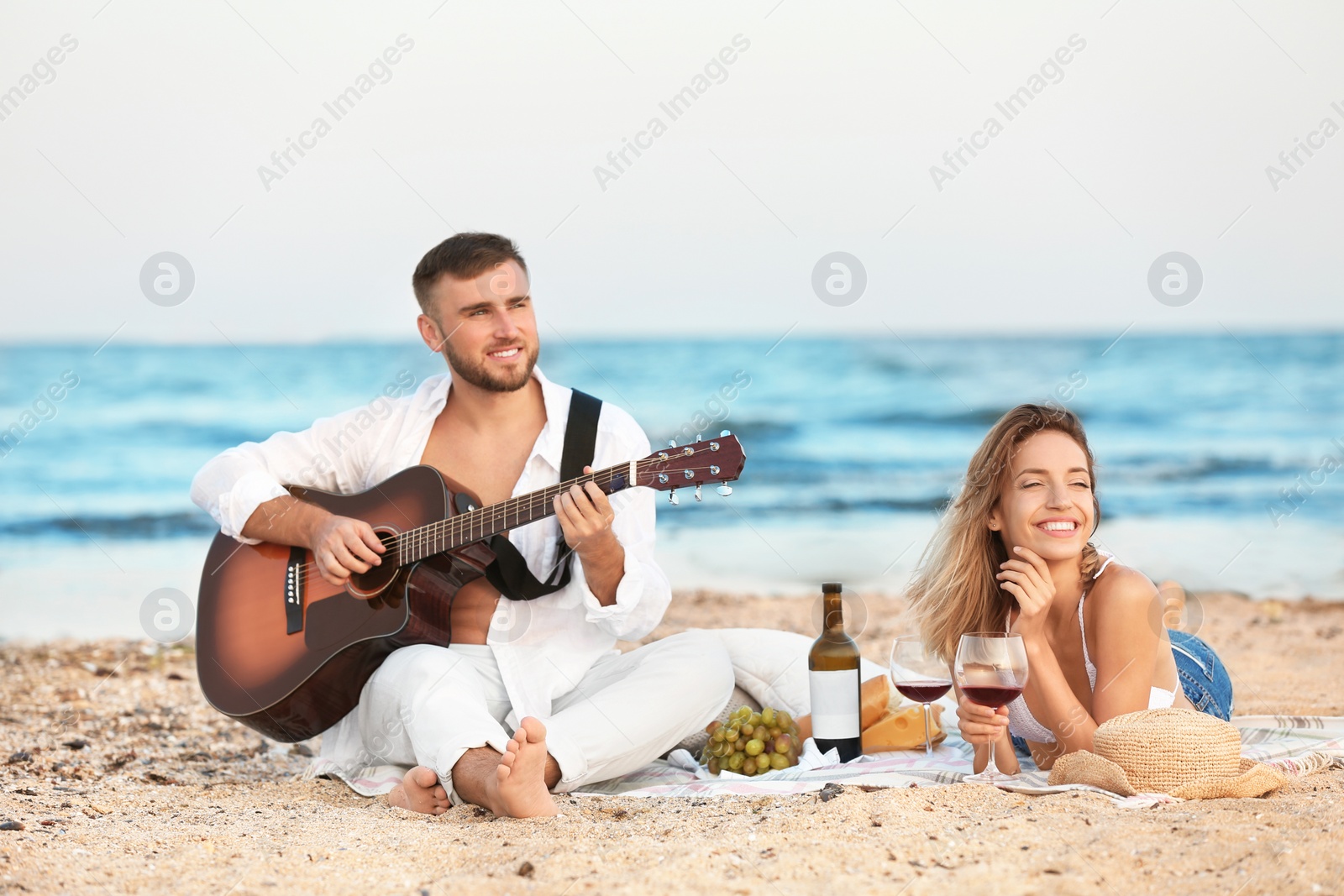 Photo of Young couple with guitar having romantic dinner on beach