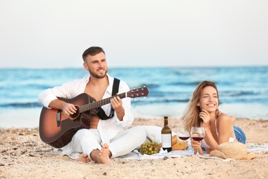 Young couple with guitar having romantic dinner on beach