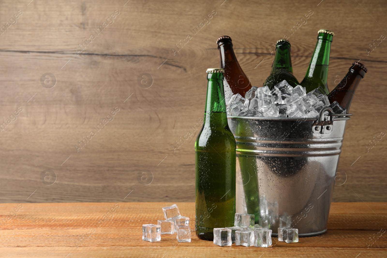 Photo of Metal bucket with beer and ice cubes on wooden background. Space for text