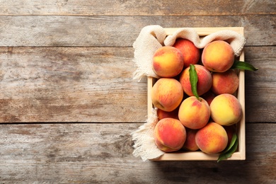 Wooden crate with fresh sweet peaches on table, top view